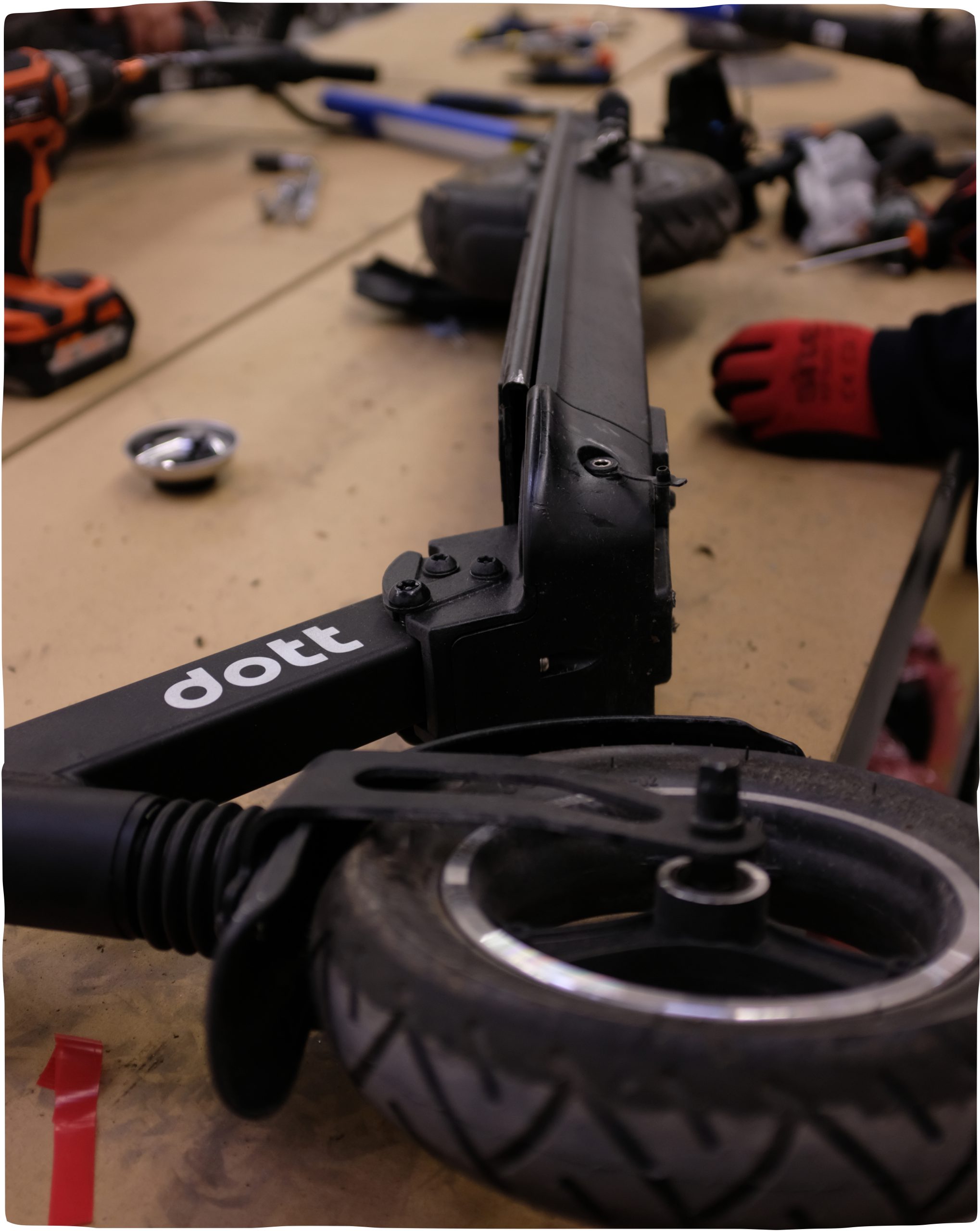 A Dott e-scooter is lying on its side and being deconstructed for repair, with a variety of tools and parts lying around it.